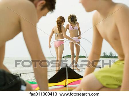 Stock Image - Boys preparing kite on beach, girls with hoola hoops in background. Fotosearch