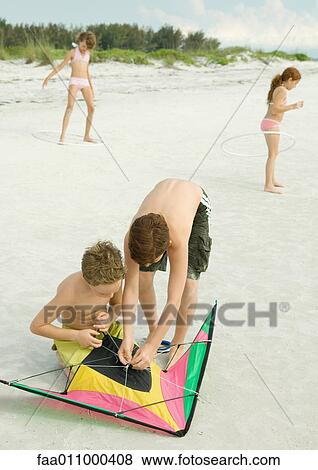 Stock Photo - Boys preparing kite on beach. Fotosearch