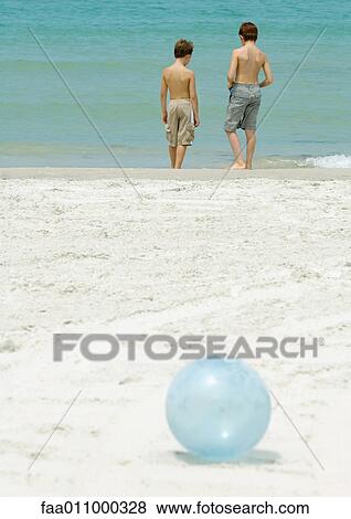 Stock Photo - Boys standing near surf, ball in foreground. Fotosearch