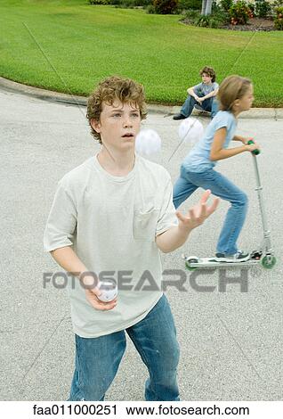 Stock Image - Children playing in suburban street, boy in foreground juggling. Fotosearch