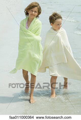 Picture - Children wrapped in towels walking in surf. Fotosearch