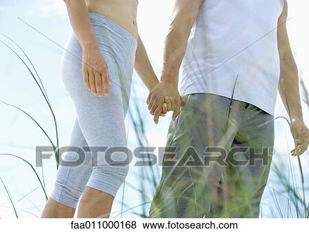 Couple walking in exercise clothes, holding hands, mid section View Large Photo Image Stock Photo - Couple walking in exercise clothes, holding hands, mid section. Fotosearch