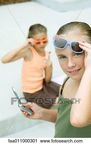 Girl lifting sunglasses and holding cell phone View Large Photo Image Stock Image - Girl lifting sunglasses and holding cell phone. Fotosearch