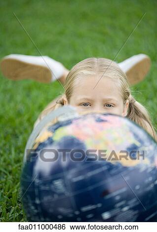 Girl lying on grass with globe, looking at camera View Large Photo Image Stock Photograph - Girl lying on grass with globe, looking at camera. Fotosearch