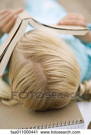 Stock Image - Girl lying with book covering face. Fotosearch