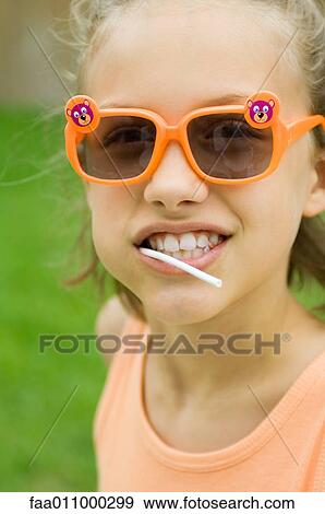 Stock Photo - Girl wearing sunglasses, lollipop in mouth, portrait. Fotosearch