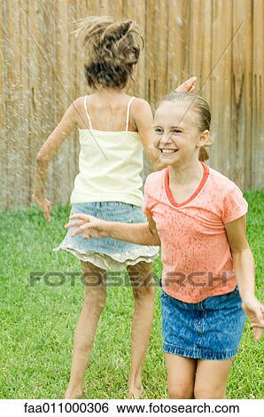 Stock Photograph - Girls jumping in sprinkler. Fotosearch