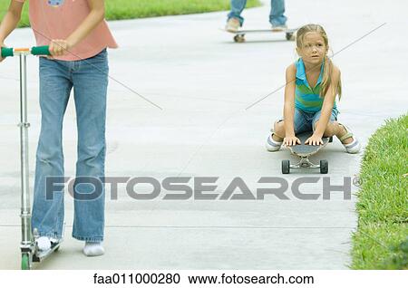 Stock Image - Kids riding scooters and skateboards in driveway. Fotosearch