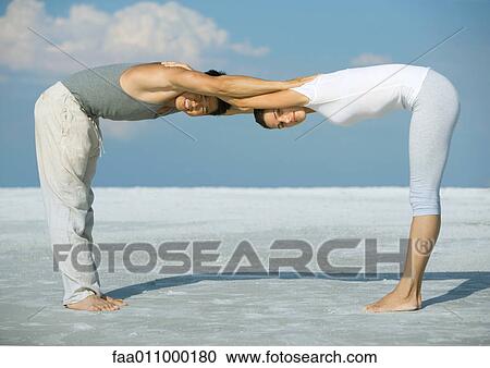 Stock Image - Man and woman bending over, head to head, arms together, on beach. Fotosearch