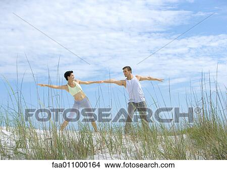 Picture - Man and woman doing side stretches on beach. Fotosearch