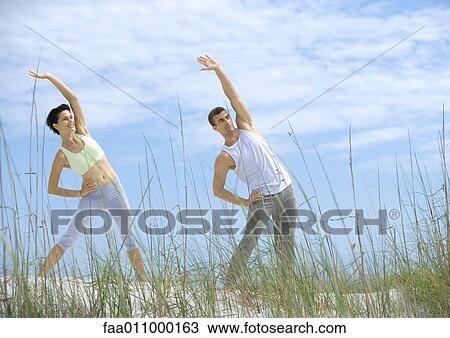 Man and woman doing side stretches on beach View Large Photo Image Stock Image - Man and woman doing side stretches on beach. Fotosearch