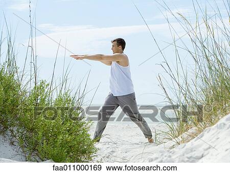 Stock Photo - Man doing stretches on beach. Fotosearch