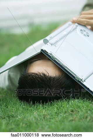 Stock Photo - Man lying in grass with laptop covering face. Fotosearch