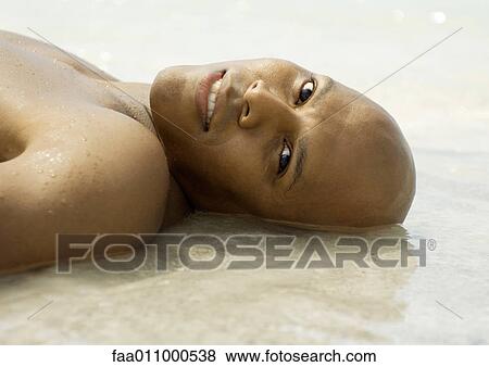 Stock Photo - Man lying in shallow water on beach, looking at camera. Fotosearch
