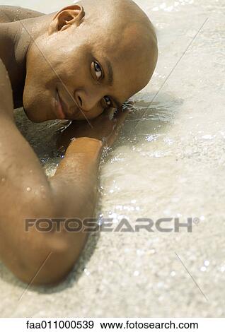 Man lying in shallow water on beach, looking at camera View Large Photo Image Stock Photo - Man lying in shallow water on beach, looking at camera. Fotosearch