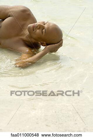 Man lying in shallow water with eyes closed View Large Photo Image Stock Photo - Man lying in shallow water with eyes closed. Fotosearch