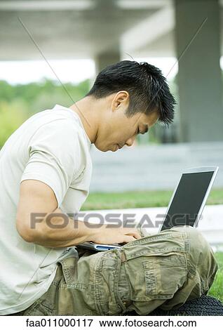 Stock Photo - Man sitting in grass using laptop. Fotosearch