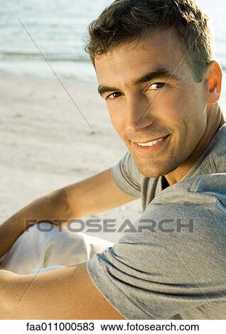 Stock Image - Man sitting on beach, portrait. Fotosearch