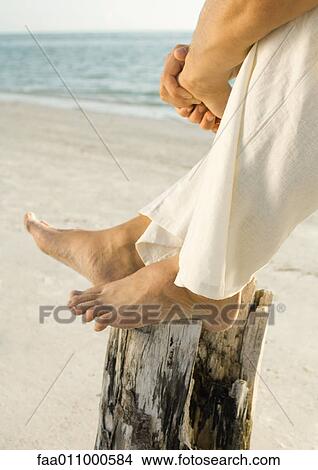 Man sitting on beach with feet on wooden post, low section View Large Photo Image Picture - Man sitting on beach with feet on wooden post, low section. Fotosearch