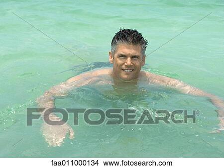 Picture - Mature man wading in sea, smiling. Fotosearch