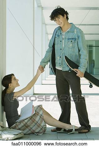 On campus, female student sitting on ground shakes hands with male student, standing with skateboard View Large Photo Image Stock Photograph - On campus, female student sitting on ground shakes hands with male student, standing with skateboard. Fotosearch