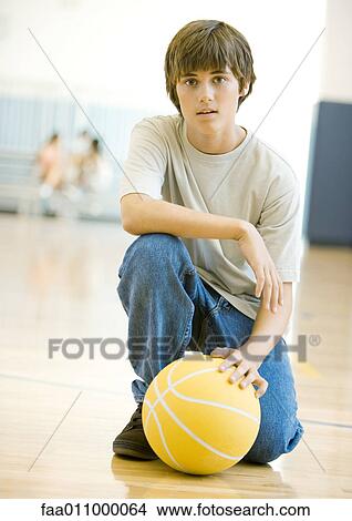Picture - Teen boy crouching with basketball in school gym. Fotosearch