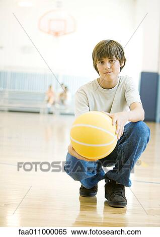 Stock Photography - Teen boy crouching with basketball in school gym. Fotosearch