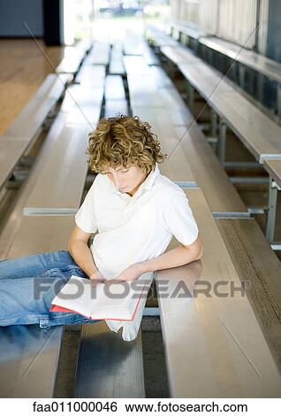 Stock Photograph - Teen boy reading book on bleachers. Fotosearch