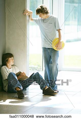 Teen boy with basketball approaching second boy studying in hallway View Large Photo Image Stock Photo - Teen boy with basketball approaching second boy studying in hallway. Fotosearch