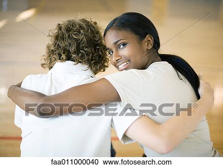 Stock Image - Teen couple sitting with arms around each other's shoulders. Fotosearch