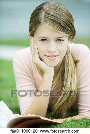 Stock Image - Teen girl lying in grass with book. Fotosearch