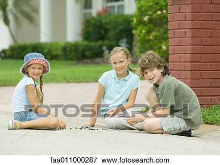 Stock Photo - Three children playing marbles outdoors. Fotosearch