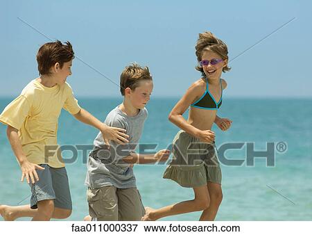 Stock Photo - Three children running next to surf on beach. Fotosearch