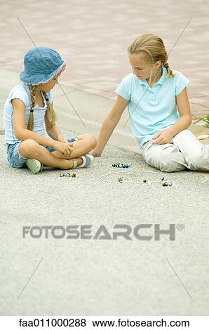 Stock Photo - Two girls playing marbles in street. Fotosearch