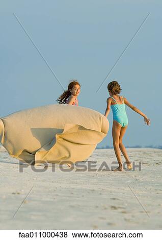 Stock Photo - Two girls running on beach, holding blanket out in wind. Fotosearch