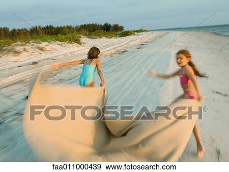 Two girls running on beach, holding blanket out in wind View Large Photo Image Stock Photo - Two girls running on beach, holding blanket out in wind. Fotosearch