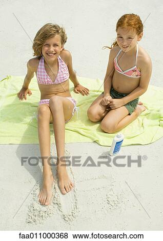 Stock Photo - Two girls sitting on towel on beach, high angle view. Fotosearch