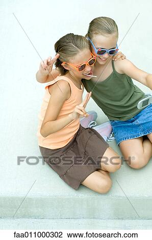 Stock Image - Two girls taking photo of selves with camera phone. Fotosearch