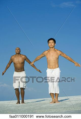 Stock Image - Two men doing relaxation exercises on the beach. Fotosearch