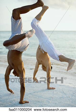Picture - Two men turning cartwheels on beach. Fotosearch