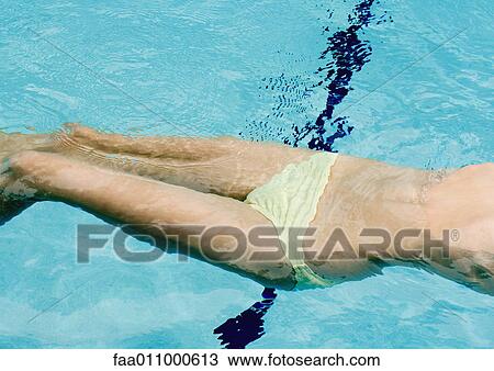 Stock Image - Woman floating on back in pool, mid section. Fotosearch