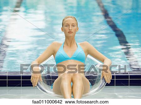 Woman in bikini sitting in transparent chair by pool View Large Photo Image Stock Image - Woman in bikini sitting in transparent chair by pool. Fotosearch