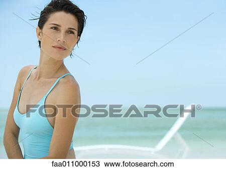 Stock Image - Woman on beach, lounge chair in background. Fotosearch