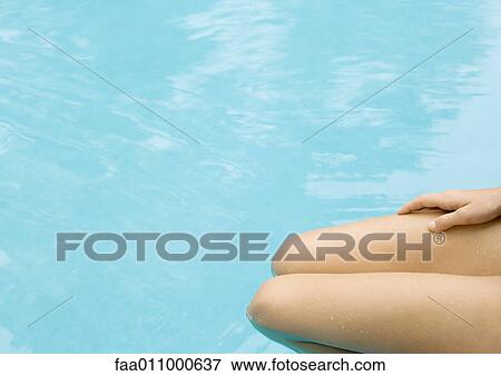 Stock Photo - Woman sitting with legs in pool, cropped view of legs. Fotosearch