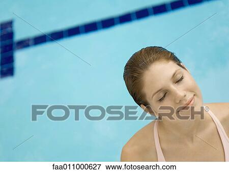 Stock Photo - Woman standing by pool, eyes closed and head tilted. Fotosearch
