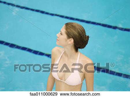 Stock Photo - Woman standing in pool by pool, looking to the side, high angle view. Fotosearch