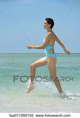 Stock Photography - Woman walking in surf, side view. Fotosearch