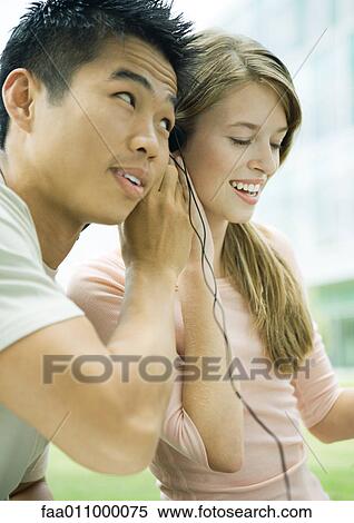 Young man and woman sharing earphones View Large Photo Image Stock Photography - Young man and woman sharing earphones. Fotosearch