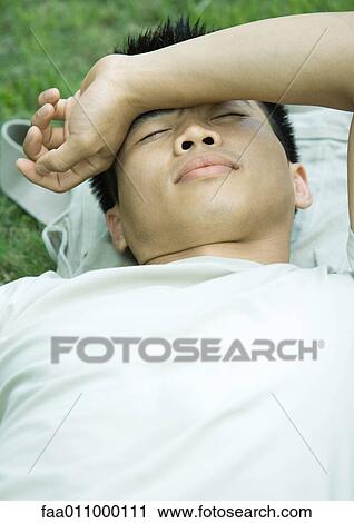 Young man lying in grass with arm across forehead View Large Photo Image Stock Image - Young man lying in grass with arm across forehead. Fotosearch