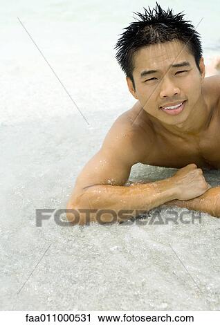 Young man lying in surf View Large Photo Image Stock Image - Young man lying in surf. Fotosearch